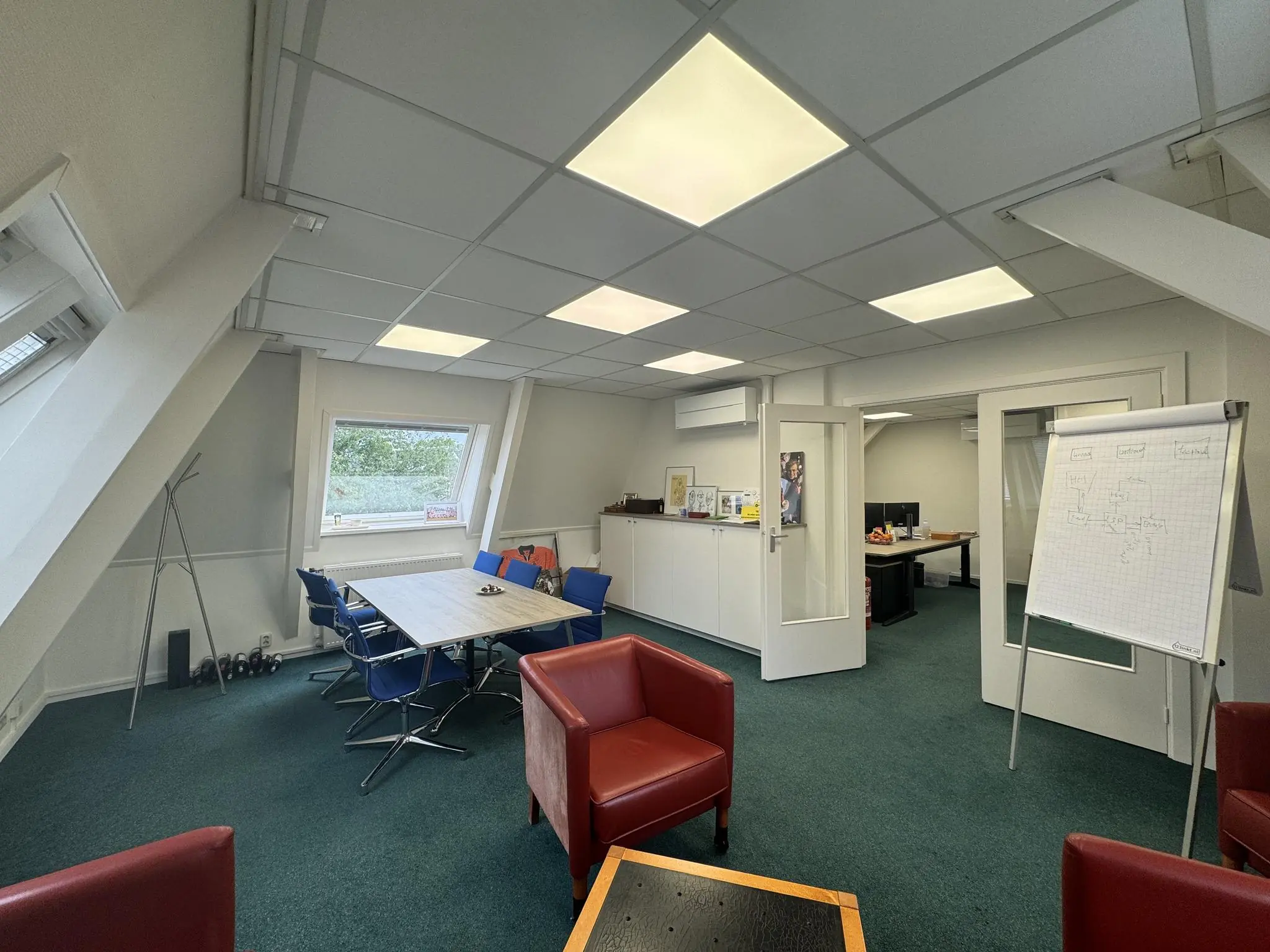 Kantoorruimte aan de Dorpsstraat met vergadertafel, flip-over en werkplekken op de achtergrond.